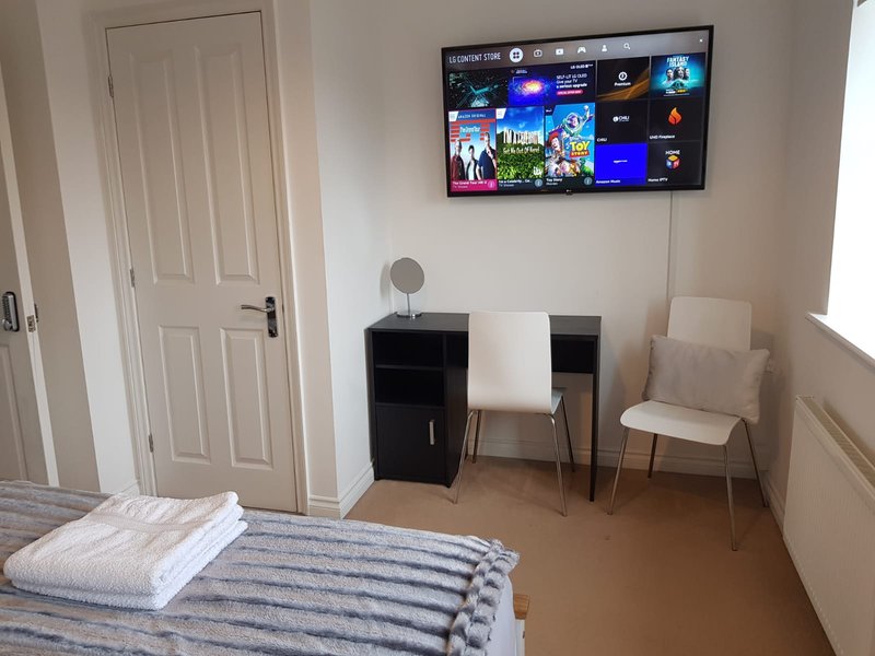 Bedroom with bed, desk, chair, wall-mounted TV and door to hallway