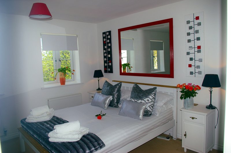 Bright bedroom with double bed, red-framed mirror, window, and bedside lamps