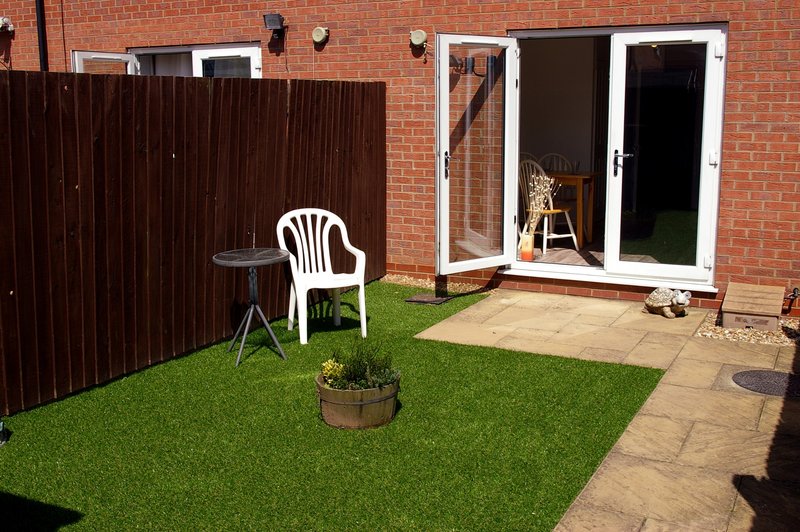 Garden patio area with artificial grass, white plastic chair, potted plants and brick house