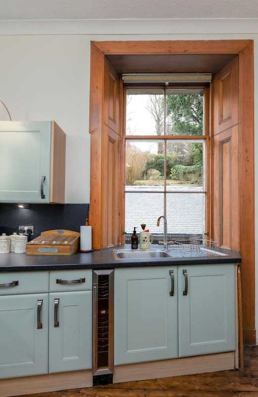 Kitchen with light blue cabinetry, dark countertop, and large wooden-framed window overlooking water