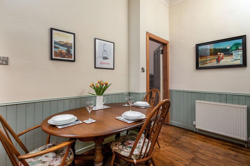 Dining room with oval wooden table, two chairs, framed wall art and flowers in vase