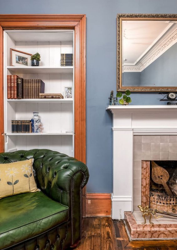 Living room with green leather sofa, wooden bookshelf, fireplace, and framed mirror on blue wall