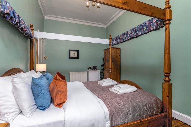 Bedroom with four-poster wooden bed, green walls, white pillows and folded towels