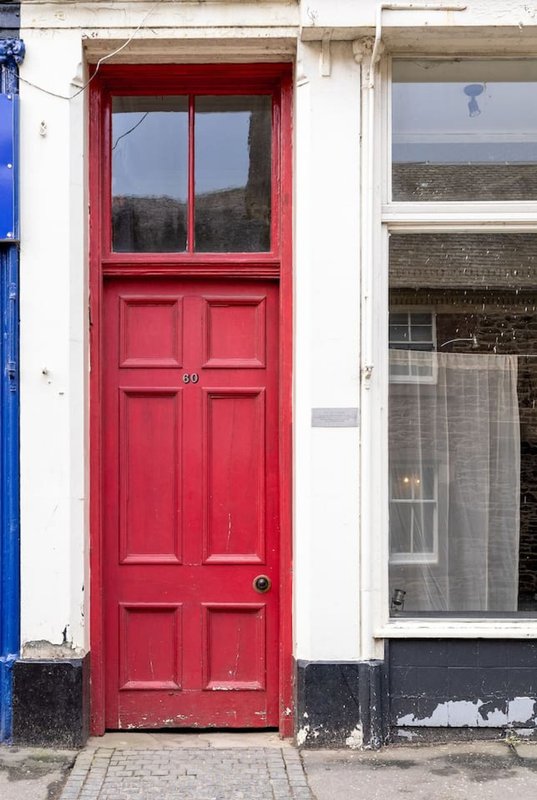 Narrow terraced house exterior with bright red door and white-painted facade