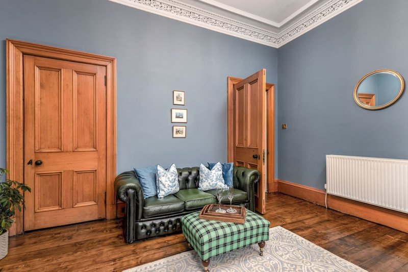 Living room with green leather Chesterfield sofa, checkered ottoman, wooden doors and parquet flooring