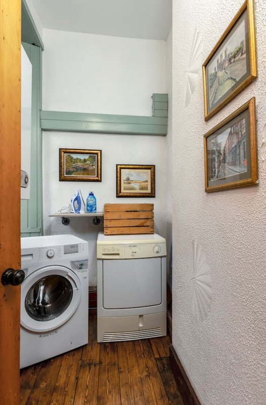 Compact laundry room with washing machine, dryer, wooden shelving, and framed wall art