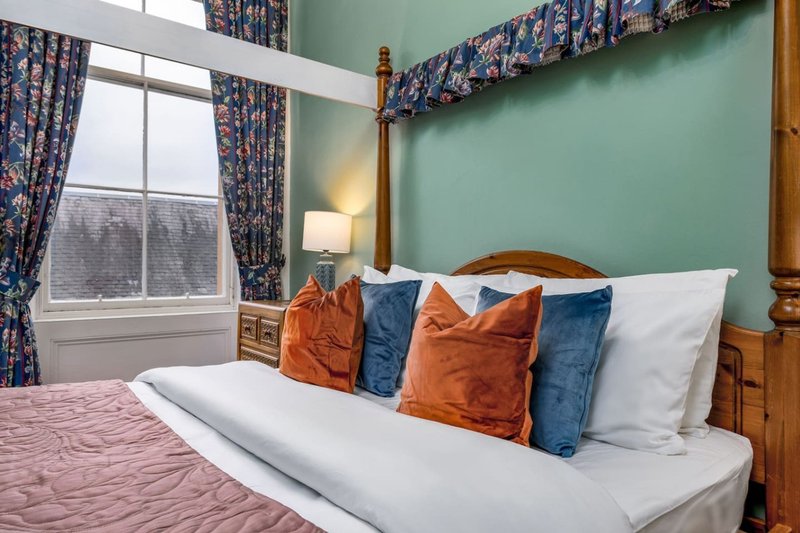 Bright bedroom with double bed, colorful cushions, mint green walls, and patterned curtains