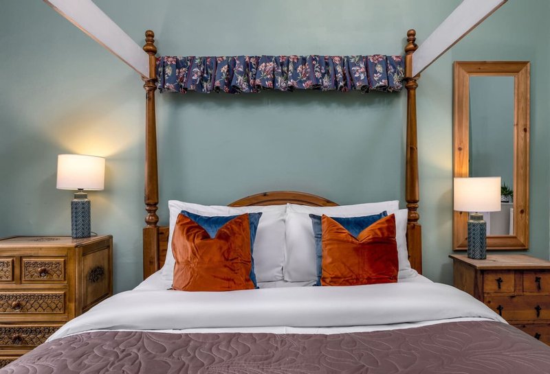 Bedroom with four-poster bed, blue walls, orange velvet pillows, wooden nightstands and lamps