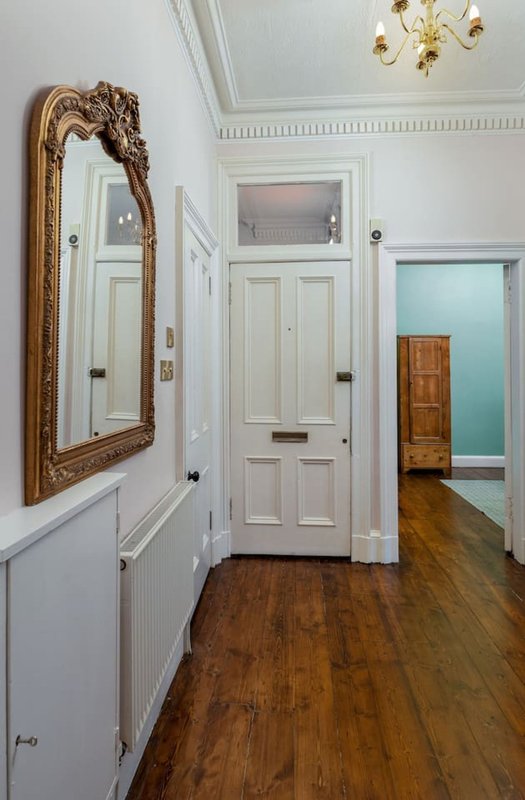 Hallway with ornate gold-framed mirror, white panelled doors, wooden flooring and ceiling rose