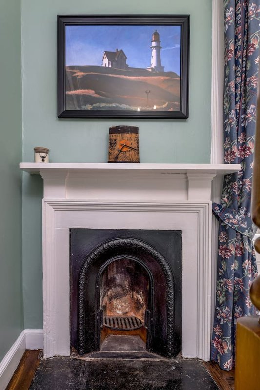 Fireplace with white mantelpiece, framed lighthouse artwork above, and decorative items on shelf