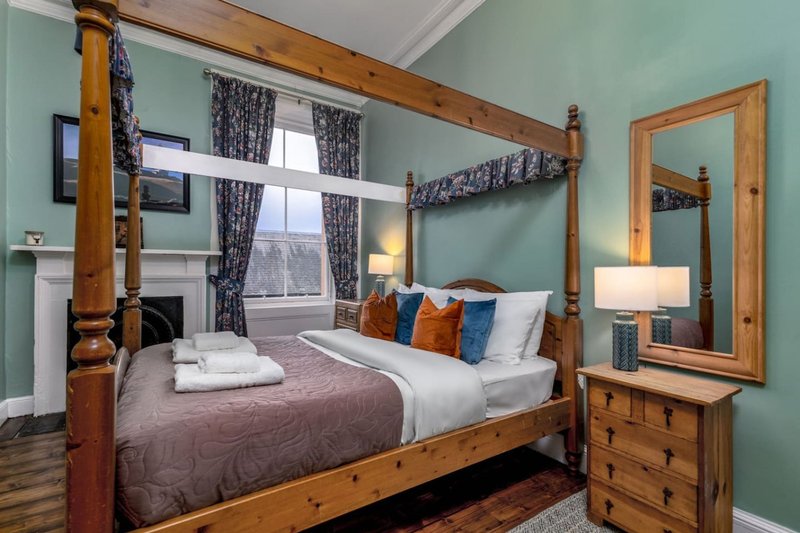 Bedroom with wooden four-poster bed, turquoise walls, large window with curtains, and wooden furniture