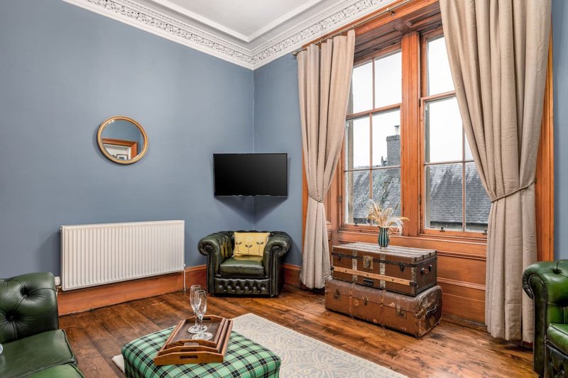 Living room with blue walls, wooden floor, leather armchair, TV, vintage suitcases and large windows
