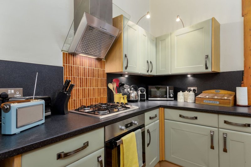 Modern kitchen with cream cabinets, black countertop, gas hob, and stainless steel extractor hood
