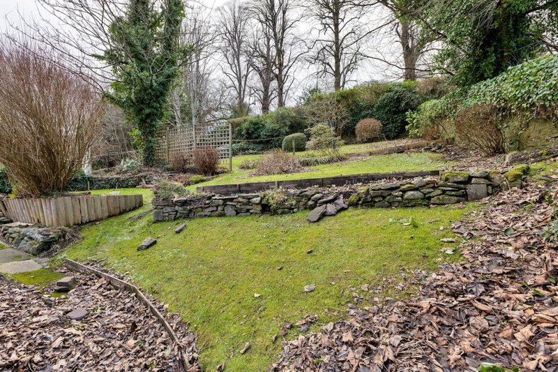 Garden exterior with lawn, stone wall, trees, and wooden fence in background