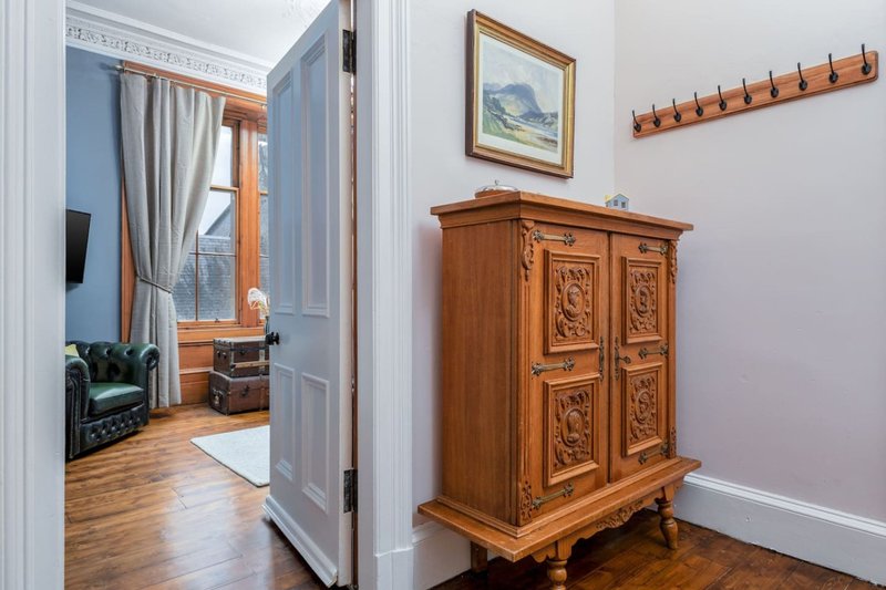 Hallway with wooden carved cabinet, framed landscape art, and open doorway to bedroom with window