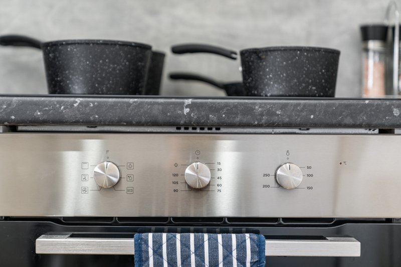 Kitchen stovetop with black speckled pots, stainless steel controls and blue striped towel