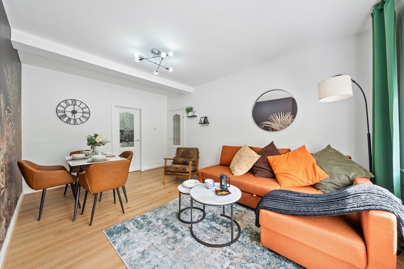 Modern living room with orange sofa, dining table, wooden floors and green curtains