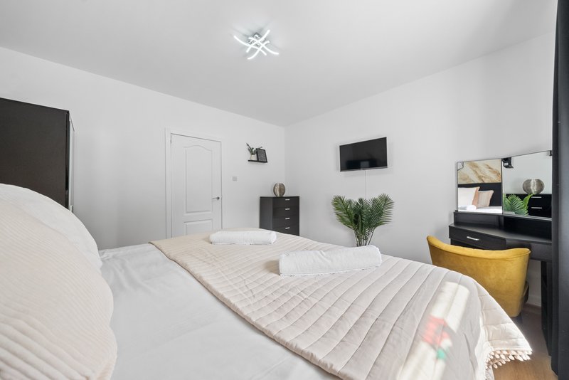 Modern bedroom with two beds, white walls, black furniture, wall-mounted TV and potted plant