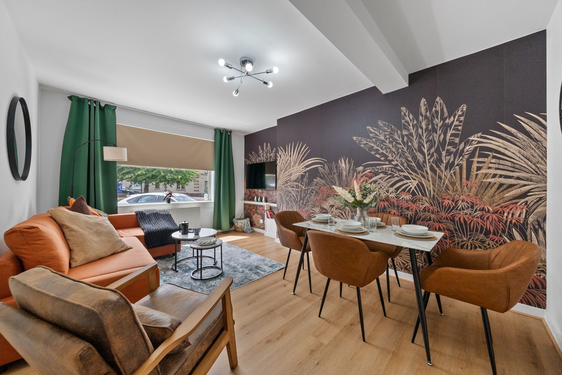Open-plan living and dining area with cognac leather furniture, botanical wall mural, and green curtains