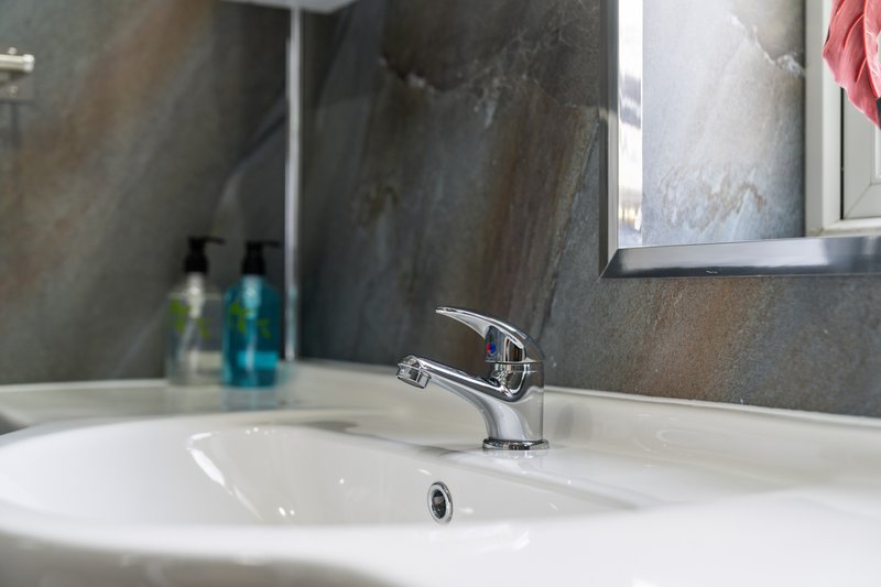 Modern bathroom sink with chrome tap, mirror and toiletries on counter