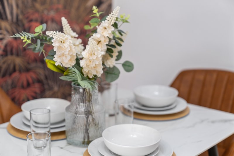 Dining table set with white plates, glasses, and cream flowers in vase