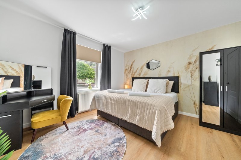 Spacious bedroom with double bed, desk, yellow chair, wooden floor and garden view