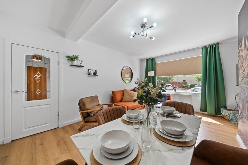 Modern open-plan dining and living room with set table, brown leather chairs and green curtains