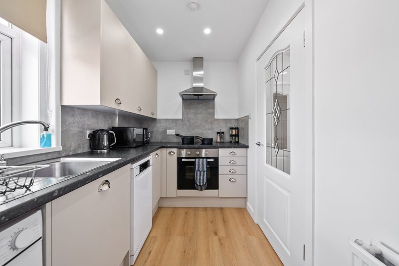 Modern galley kitchen with cream cabinets, black countertop, stainless steel appliances and wooden flooring