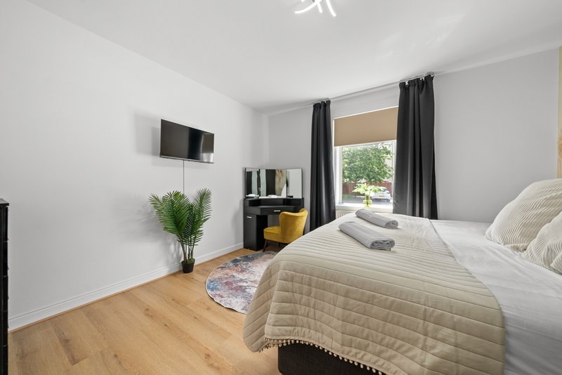 Bright modern bedroom with double bed, wall-mounted TV, wooden floor and garden view