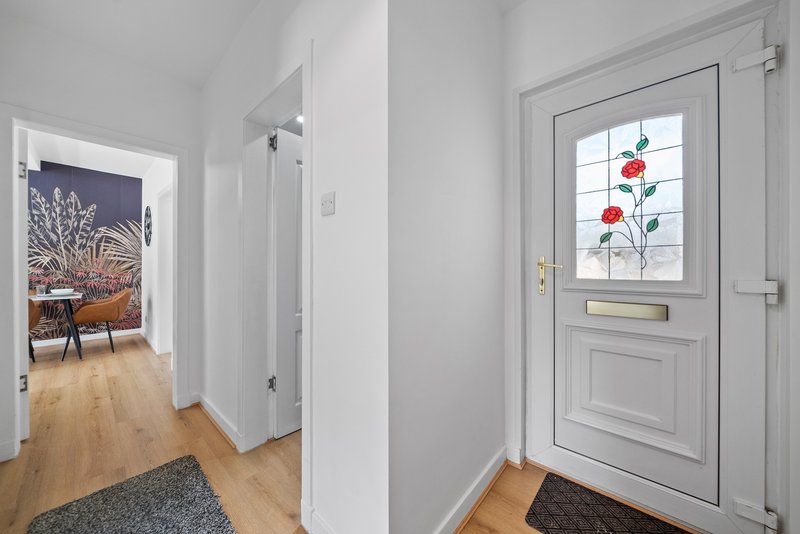 Bright entrance hallway with wooden flooring, white walls, and front door with decorative window pane