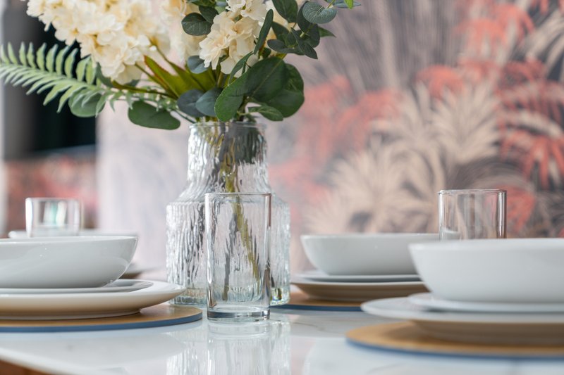 Dining table set with white bowls, gold placemats and fresh flowers in glass vase