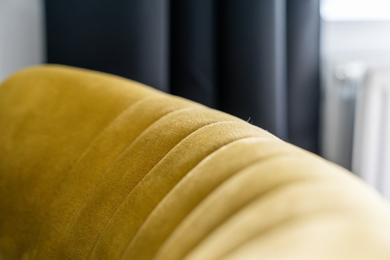 Close-up of yellow upholstered armchair with dark curtains in background