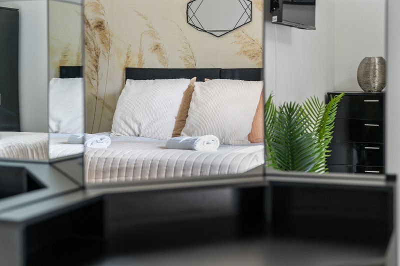 Modern bedroom with black bed frame, white bedding, dried pampas grass decor, and potted plant