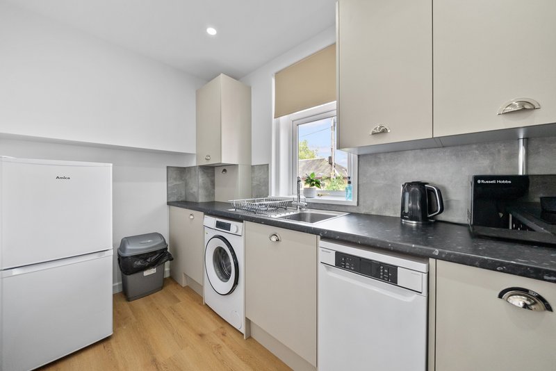 Modern kitchen with cream cabinetry, black countertops, washing machine, and stainless steel appliances