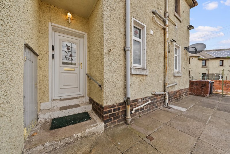 Stone-rendered terraced house exterior with cream-painted front door and paved entrance area