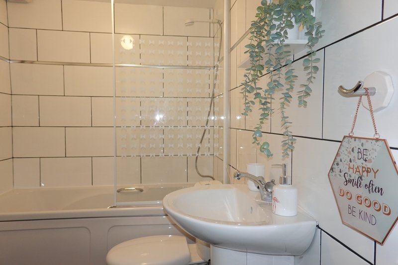 Modern bathroom with white subway tiles, glass shower enclosure, white pedestal sink and hanging plant decor
