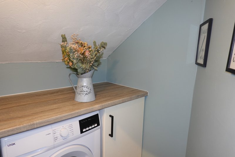Utility room with washing machine, wooden countertop, dried flowers in vase, and framed wall art