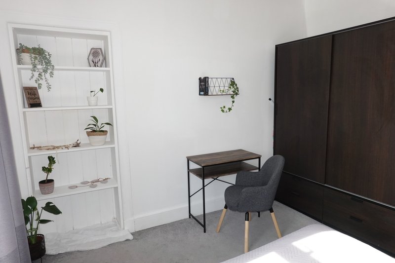 Minimalist bedroom with white shelving unit, small desk, gray chair and dark wardrobe
