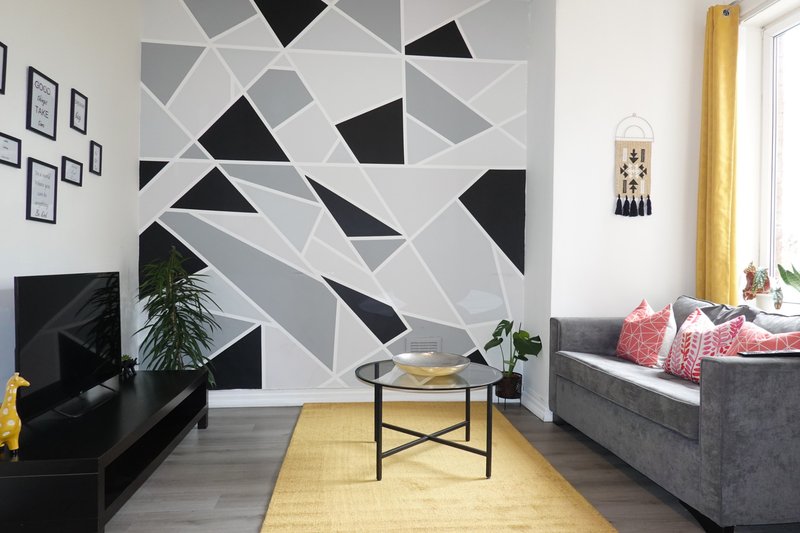 Modern living room with geometric wall art, black furniture, yellow rug and large window
