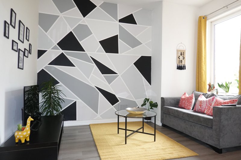Modern living room with geometric wall mural, gray sofa, yellow accents, and potted plants