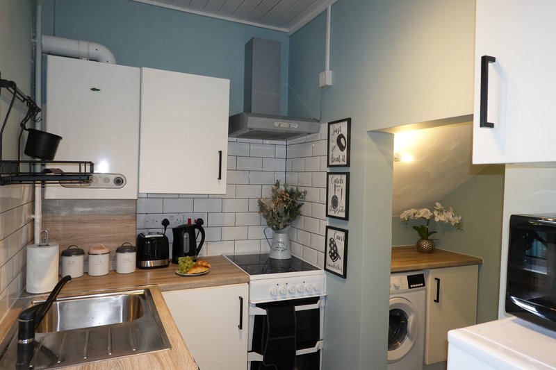 Compact kitchen with white cabinets, wooden countertop, sink, and appliances
