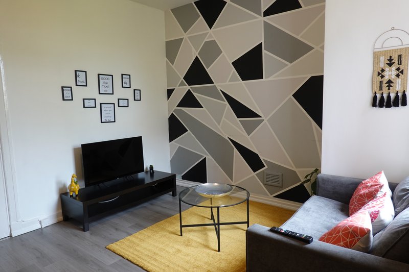 Living room with geometric wall art, TV stand, round table, sofa with cushions and yellow rug