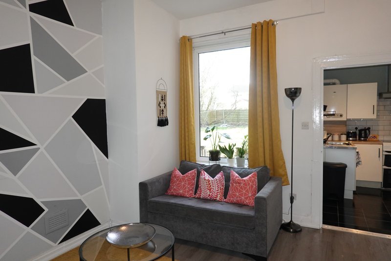 Modern living room with gray sofa, geometric wall art, gold curtains and kitchen visible