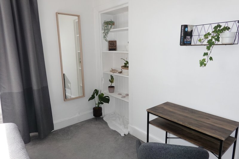 Bright bedroom corner with mirror, shelving unit, potted plants, bench seat and curtains
