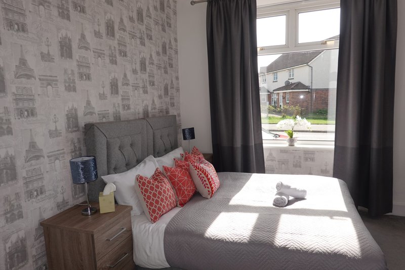 Bedroom with double bed, red cushions, grey headboard and dark curtains