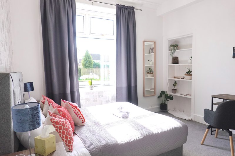 Bright bedroom with double bed, grey curtains, built-in shelving and window view