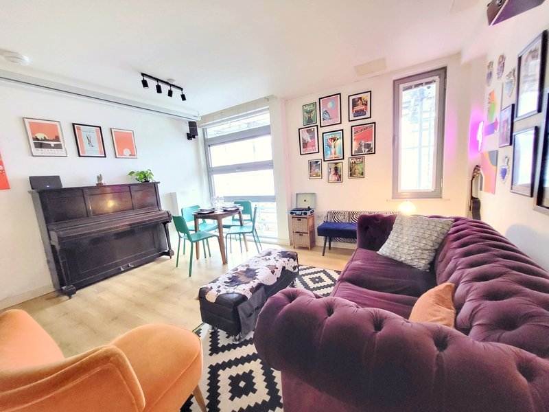 Open-plan living room with purple sofa, piano, framed wall art, and bright windows
