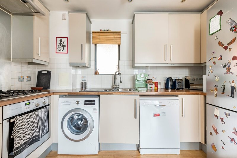 Modern kitchen with white cabinetry, wooden countertops, washing machine, dishwasher and gas hob