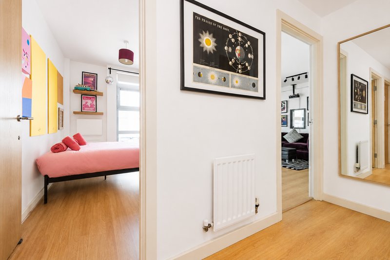 Bright hallway with wooden flooring, white walls, and open doorways leading to bedroom and bathroom areas