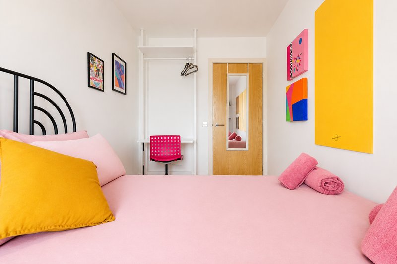 Bright modern bedroom with pink bedding, yellow pillows, colorful wall art and wooden door